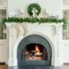 Cypress Spruce Wreath with a velvet bow displayed on a white fireplace mantel above a lit hearth.