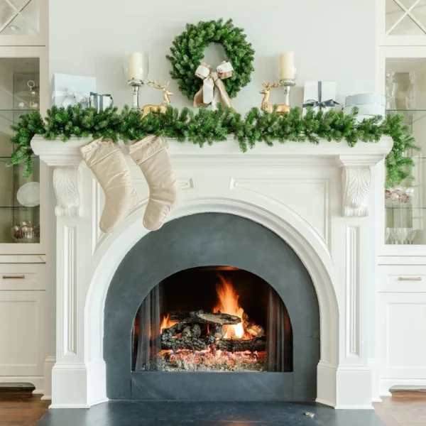 Cypress Spruce Wreath with a velvet bow displayed on a white fireplace mantel above a lit hearth.