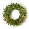 Pre-lit Cypress Spruce Wreath with full green foliage illuminated by warm mini lights on a white background.