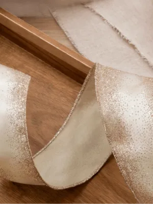 Close-up of cream-colored Gold Glitter Ribbon with shimmering gradient edges curved on a wooden tray.