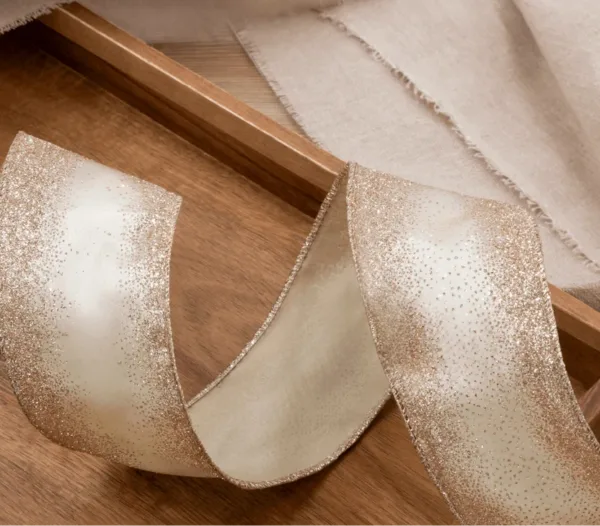 gold_gliterribbon Close-up of cream-colored Gold Glitter Ribbon with shimmering gradient edges curved on a wooden tray.