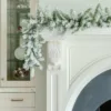 King Flock Garland with snow-dusted pine foliage cascading over the edge of a white fireplace mantel next to glass cabinetry.