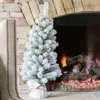 3' King Flock Artificial Christmas Tabletop Tree in a burlap base standing on a stone fireplace hearth next to a lit fire.