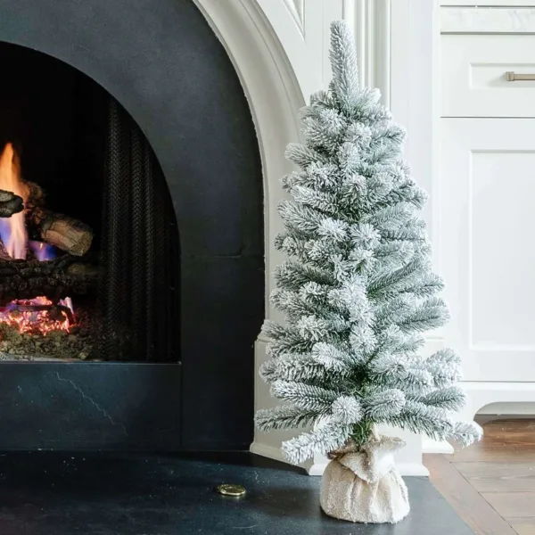 3' King Flock Artificial Christmas Tabletop Tree wrapped in burlap set beside a glowing white fireplace.