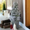 3' King Flock Artificial Christmas Tabletop Tree placed in a metal bucket on a porch next to ice skates and firewood.
