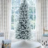 Unlit King Flock Slim Artificial Christmas Tree displayed in a sunlit room in front of a window.