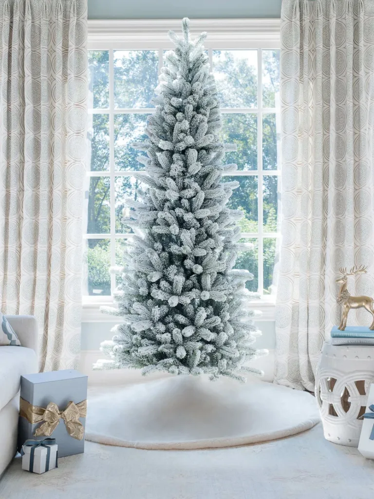 Unlit King Flock Slim Artificial Christmas Tree displayed in a sunlit room in front of a window.