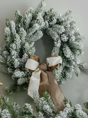 King Flock Wreath adorned with a taupe and cream velvet bow hanging above a mantel with golden reindeer figurines.