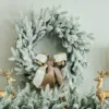 Queen Flock Wreath styled with a taupe and white velvet bow hanging above a mantel flanked by gold reindeer.