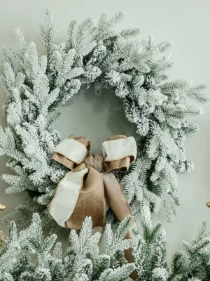 Queen Flock Wreath styled with a taupe and white velvet bow hanging above a mantel flanked by gold reindeer.