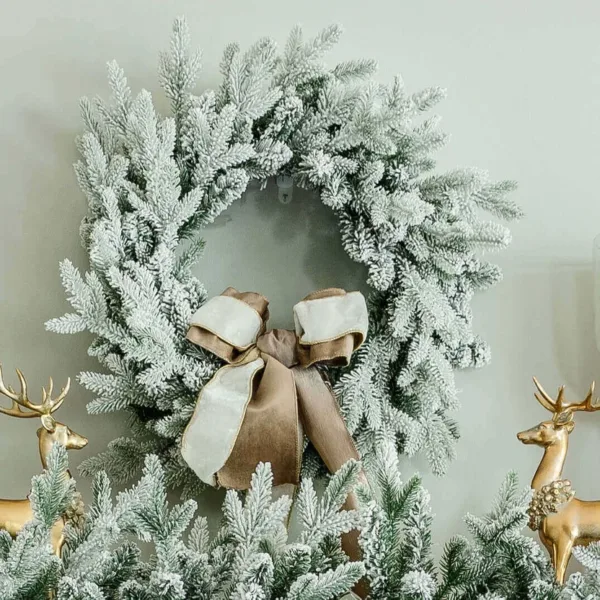 Queen Flock Wreath styled with a taupe and white velvet bow hanging above a mantel flanked by gold reindeer.