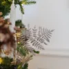 Rosegold Leaf Pick with fern-like fronds styled on a decorated Christmas tree next to ornaments.