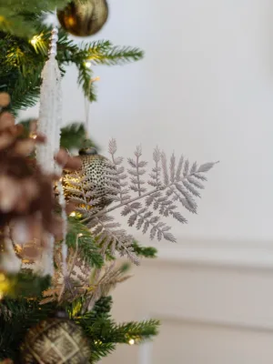 Rosegold Leaf Pick with fern-like fronds styled on a decorated Christmas tree next to ornaments.