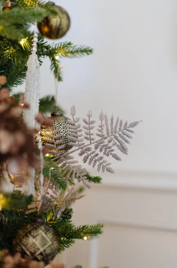 Rosegold Leaf Pick with fern-like fronds styled on a decorated Christmas tree next to ornaments.
