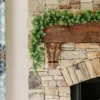 Royal Fir Garland with lush green evergreen branches draped across a rustic dark wood mantel on a stone fireplace.