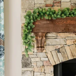 Royal Fir Garland with lush green evergreen branches draped across a rustic dark wood mantel on a stone fireplace.