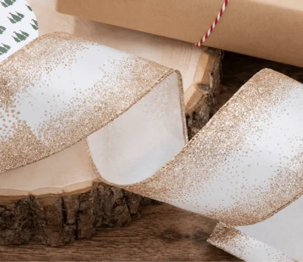 Close-up of white ribbon with gold glittery gradient edges coiled on a wood slice.